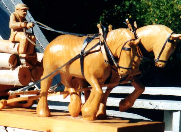 Carving of two horses pulling a wagon loaded with logs